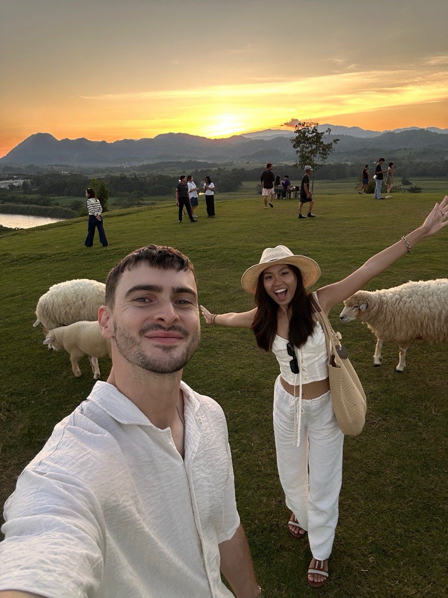 Oli and Vivi smiling in a field with sheep at sunset